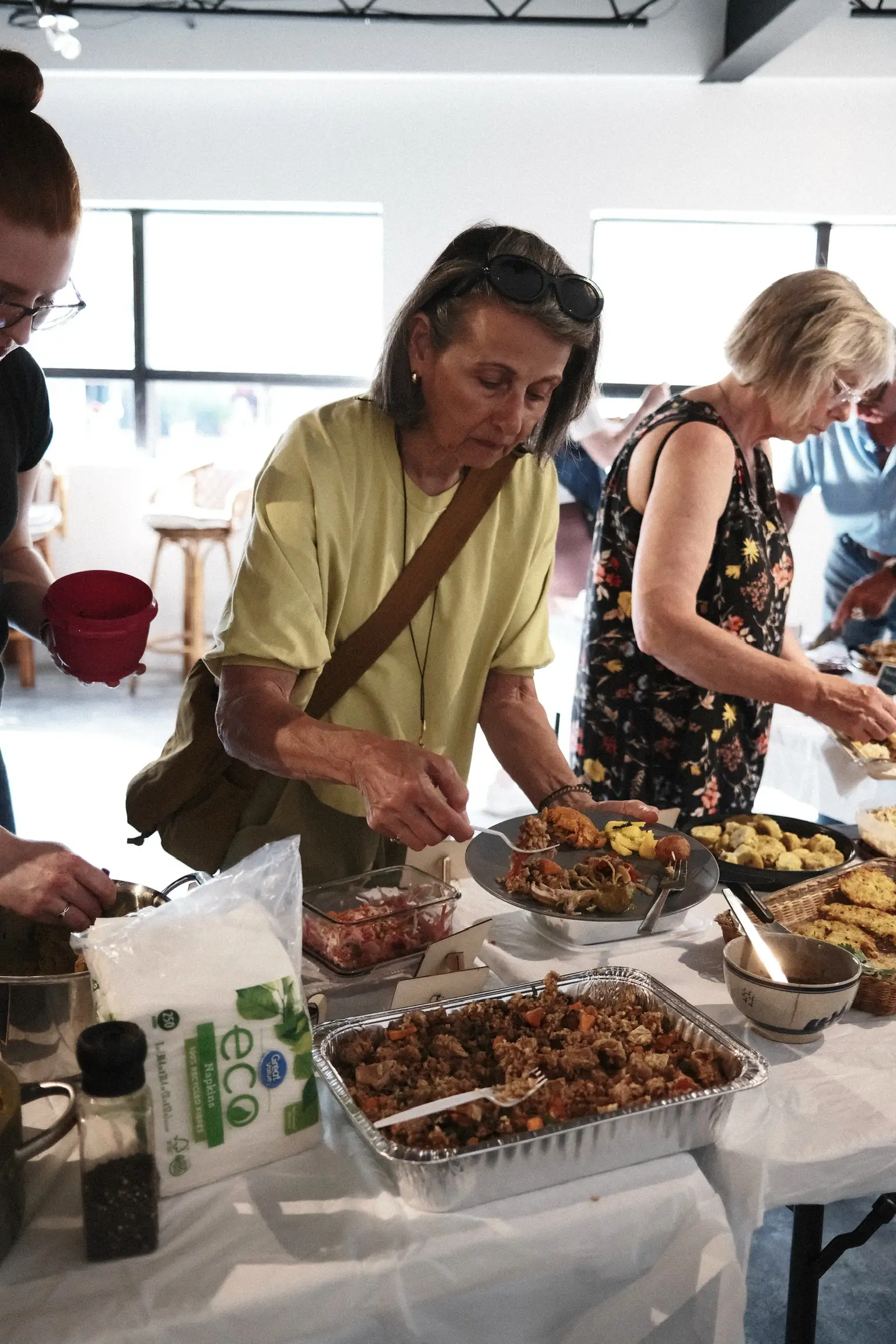A busy Sauté Sundays table, guests serving themselves from trays and glass dishes while others reach across